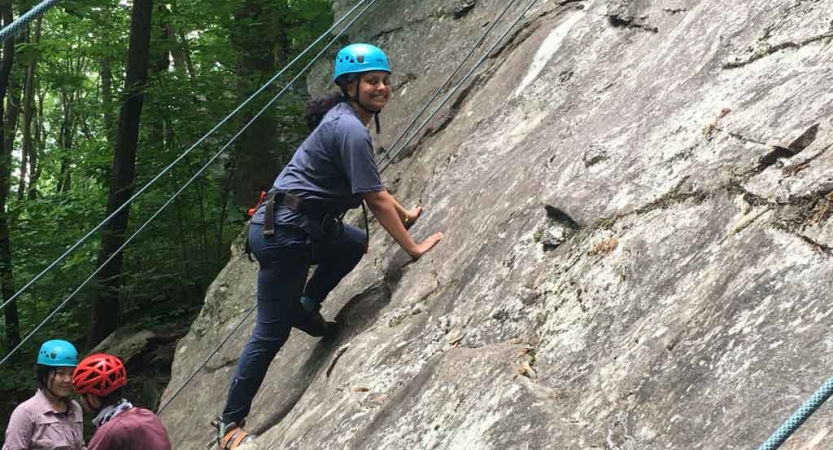 a gap year student pauses to smile at the camera while rock climbing on an outward bound course